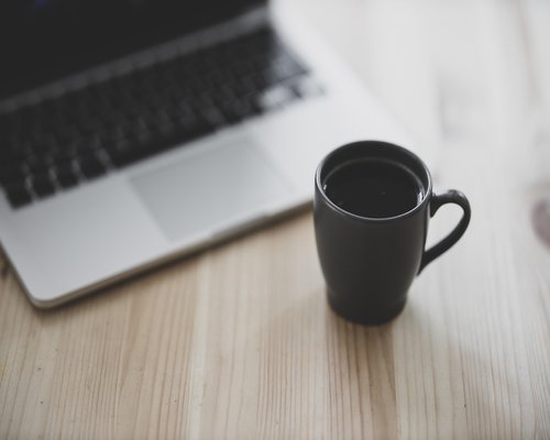 A cup of coffee next to a laptop in the morning